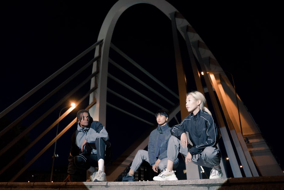 Stylish models in sportswear crouching on urban bridge at night Korean streetwear