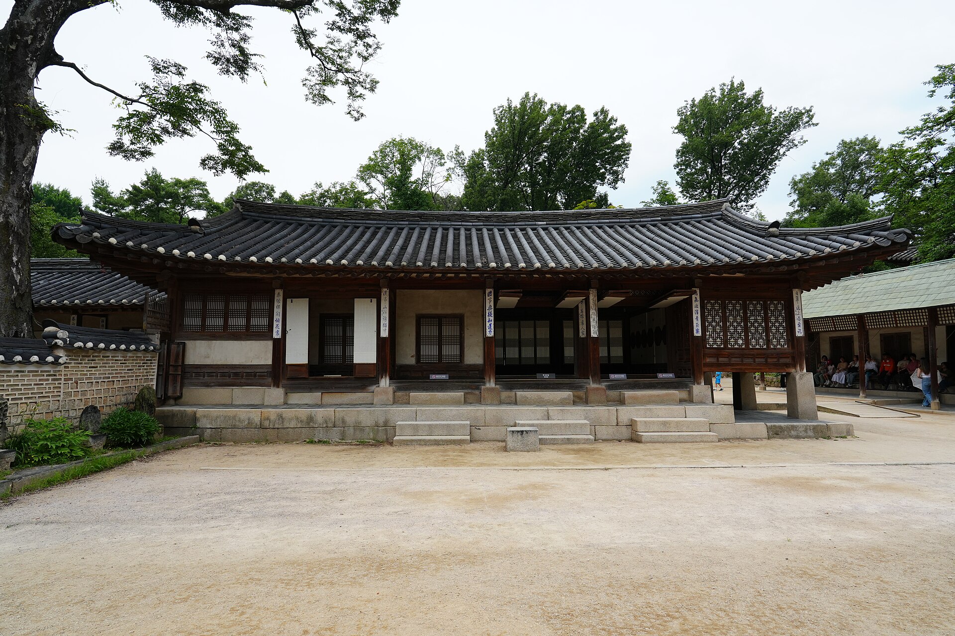 Yeongyeongdang in the Secret Garden, a long unpainted single-storey wooden house with a tiled roof and a sandy courtyard, trees behind