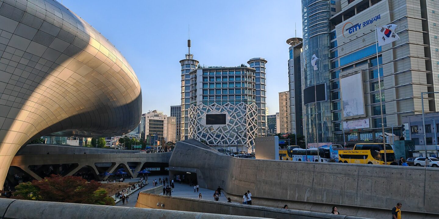 The curved silver form of Dongdaemun Design Plaza with the Dongdaemun shopping towers behind