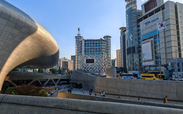 The curved silver form of Dongdaemun Design Plaza with the Dongdaemun shopping towers behind
