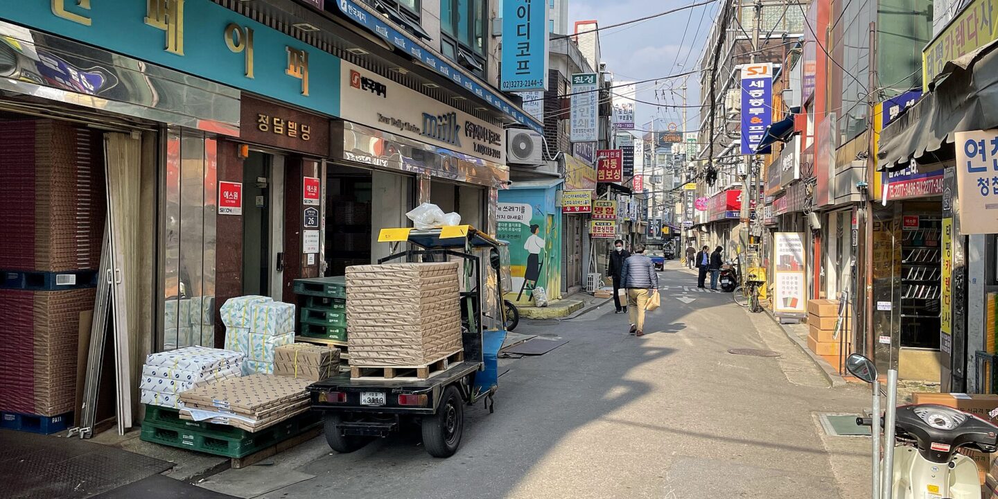 Euljiro paper wholesaler street by day with stacked paper, a loading truck and layered Korean shop signs