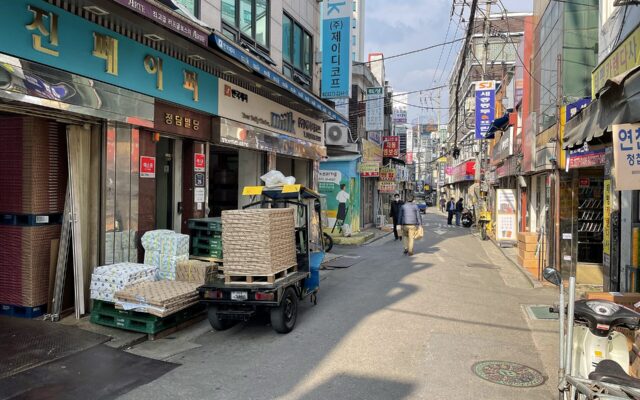 Euljiro paper wholesaler street by day with stacked paper, a loading truck and layered Korean shop signs