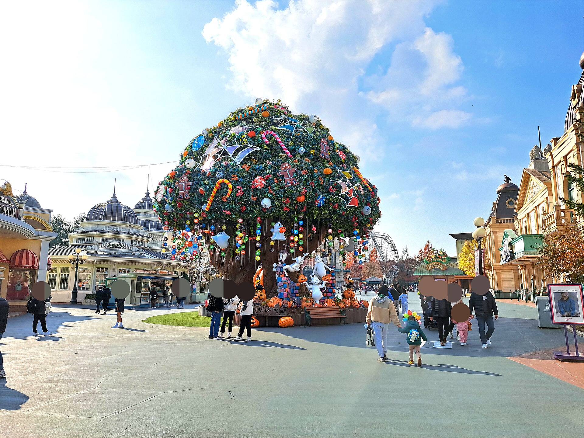 A giant decorated tree in the main plaza at Everland, with European-style buildings and a domed hall behind and visitors walking under a blue sky
