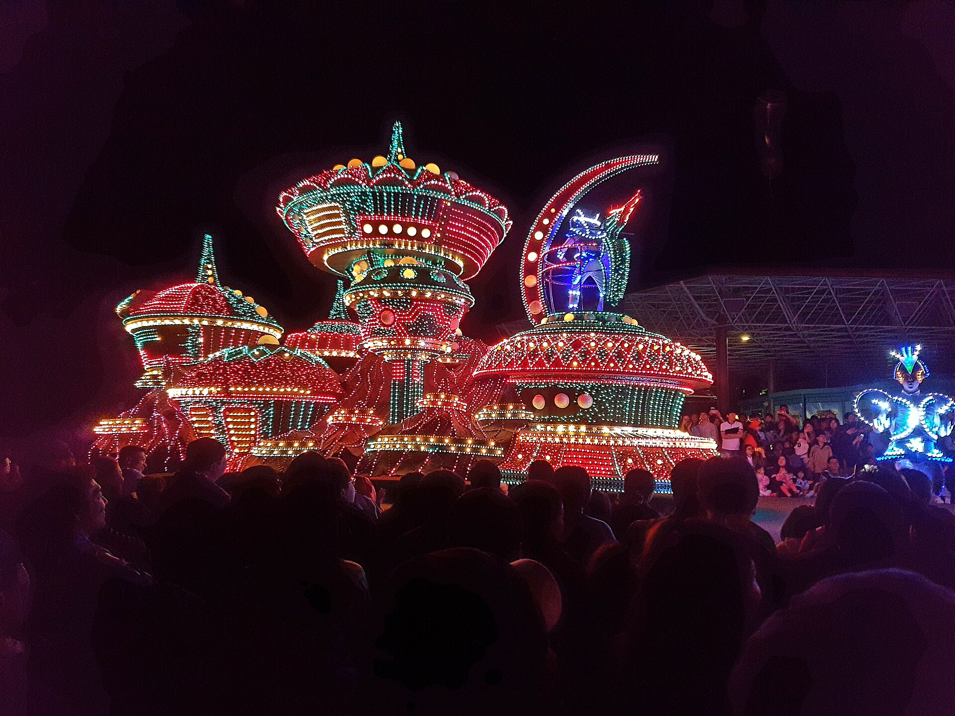 Brightly illuminated parade floats covered in coloured lights moving past a crowd at night at Everland