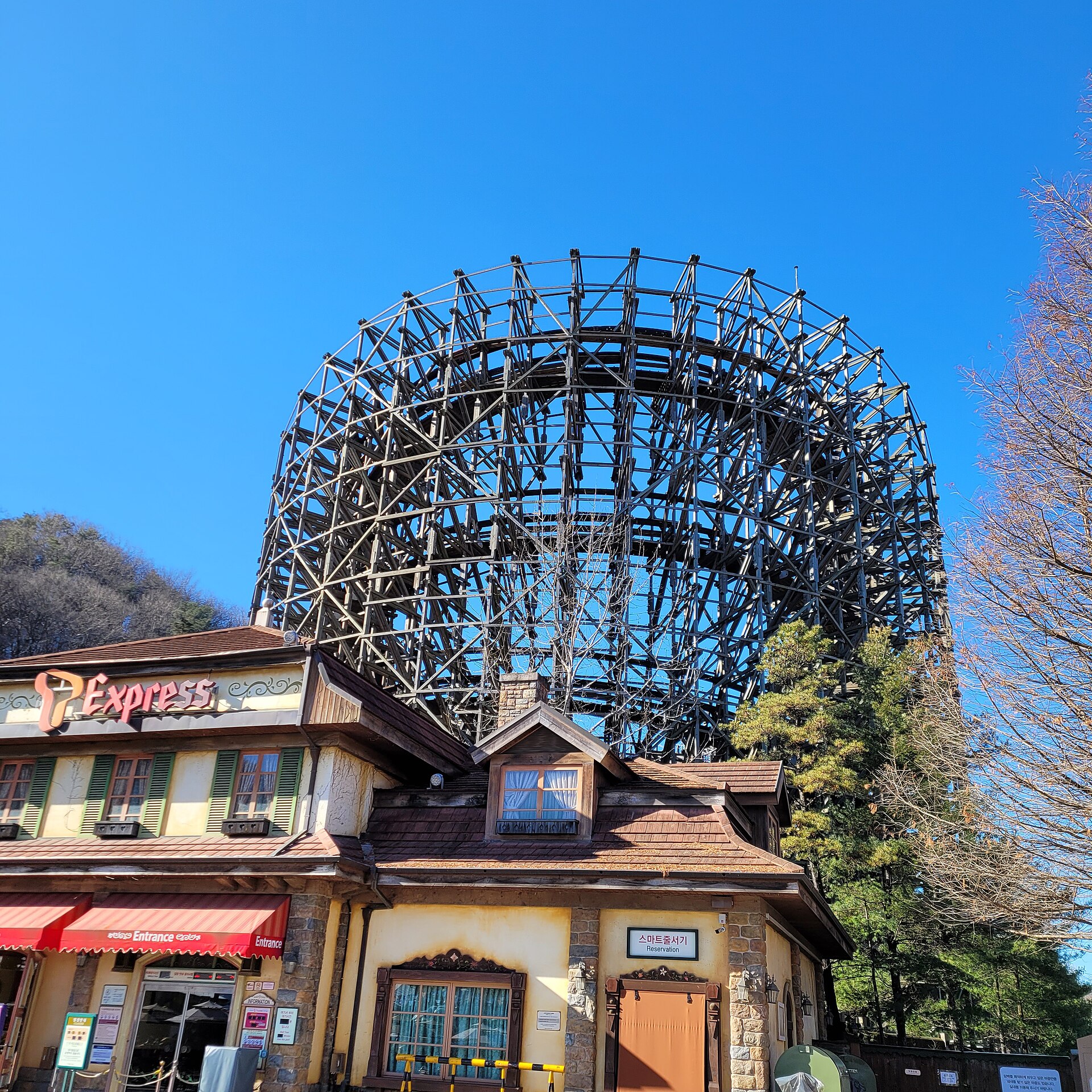 The timber lattice of the T Express wooden roller coaster rising behind its station building at Everland under a clear blue sky