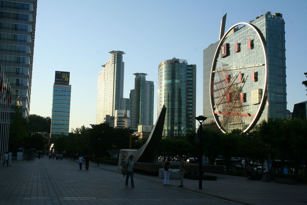 Wide paved plaza in Gangnam surrounded by glass office towers and a large circular sculpture
