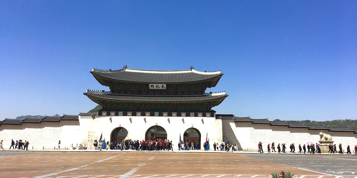 Gwanghwamun Gate of Gyeongbokgung Palace under a clear blue sky with visitors walking along the palace wall