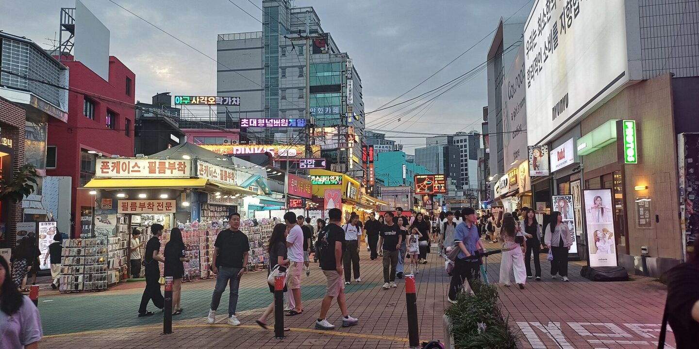 Busy Hongdae street at dusk with illuminated Korean shop signs and crowds of young people