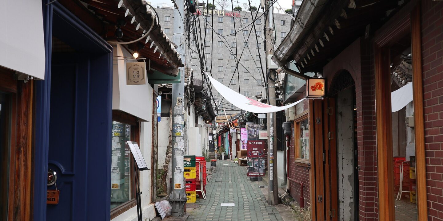 Narrow Ikseon-dong alley lined with hanok shops, tiled eaves and overhead cables with a hotel behind