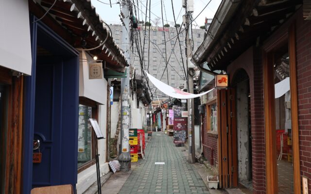 Narrow Ikseon-dong alley lined with hanok shops, tiled eaves and overhead cables with a hotel behind