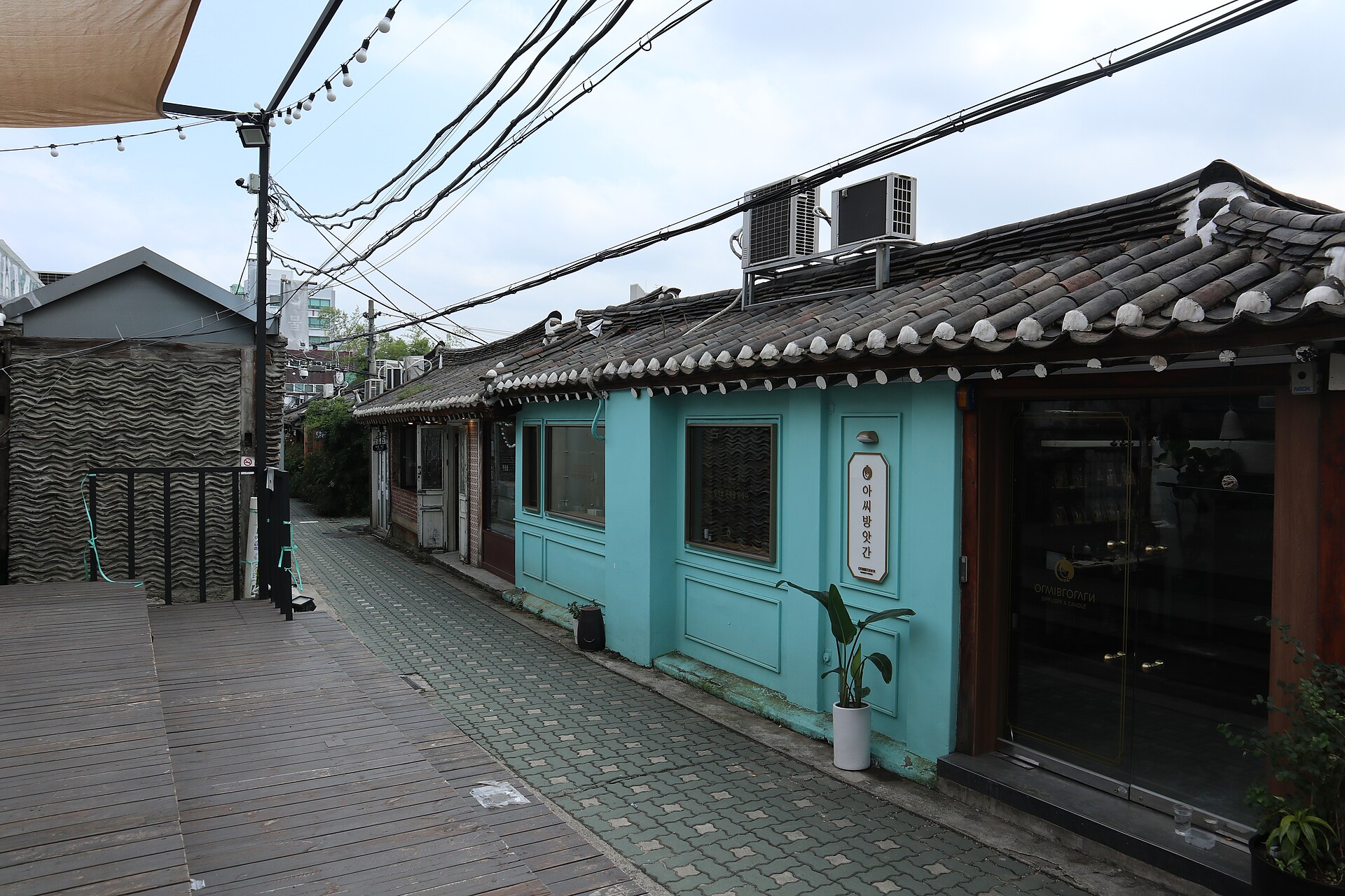 Row of low hanok shops with dark tiled roofs and a turquoise-painted facade along a paved Ikseon-dong alley