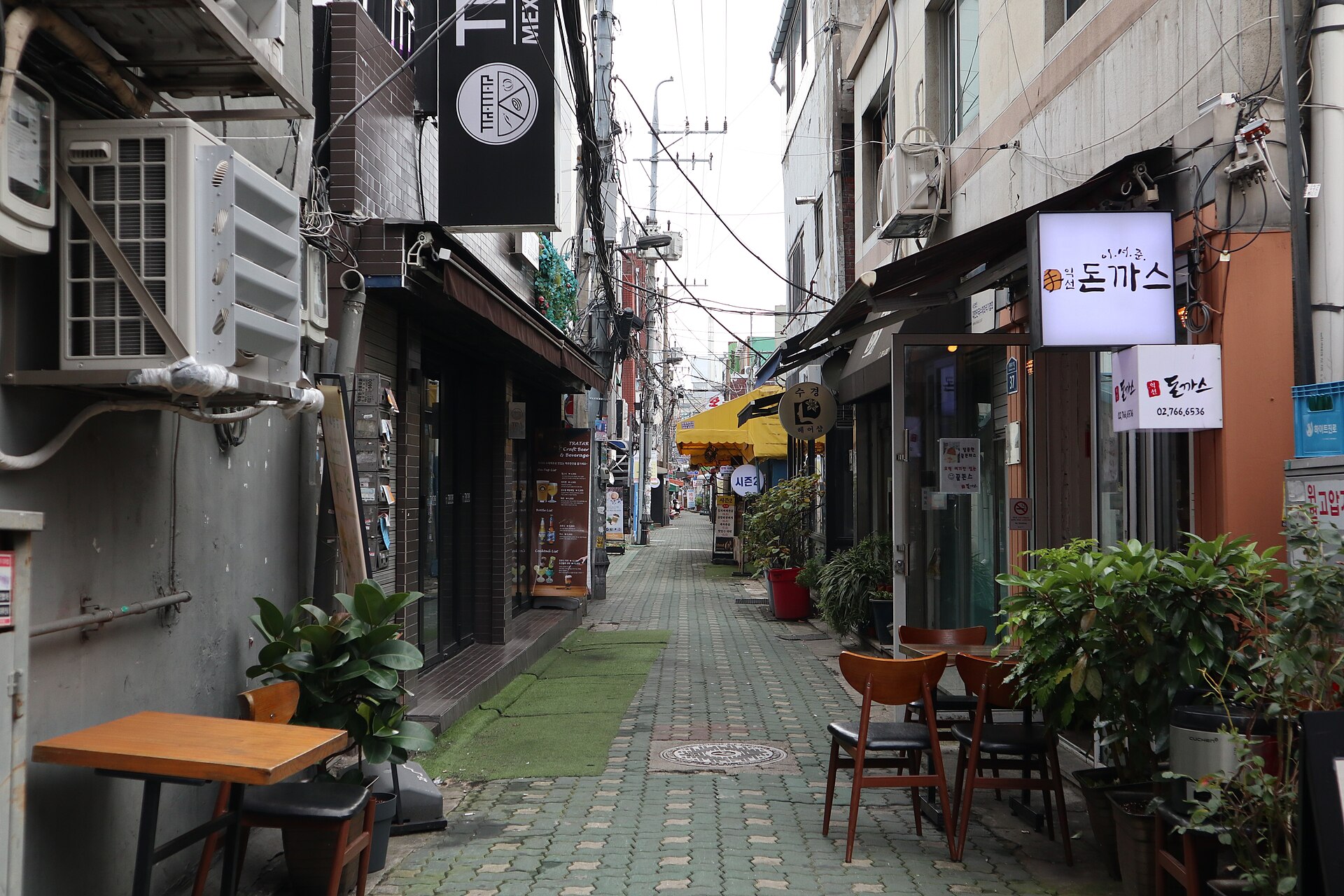 Quiet Ikseon-dong side lane with a tonkatsu restaurant sign, outdoor cafe chairs and low concrete buildings