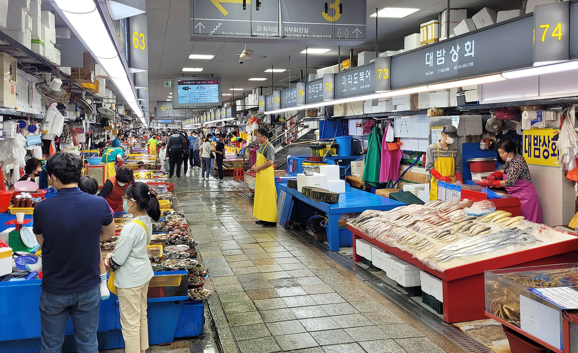 Rows of seafood stalls with vendors and shoppers inside Jagalchi fish market in Busan