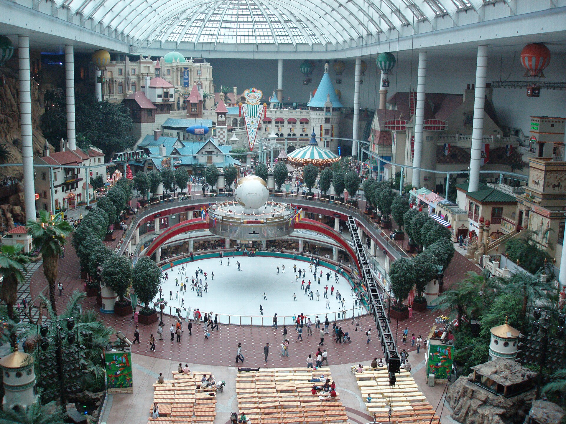 The inside of Lotte World Adventure seen from above in daylight, with an ice rink ringed by galleries and a fairy-tale village under a glass dome