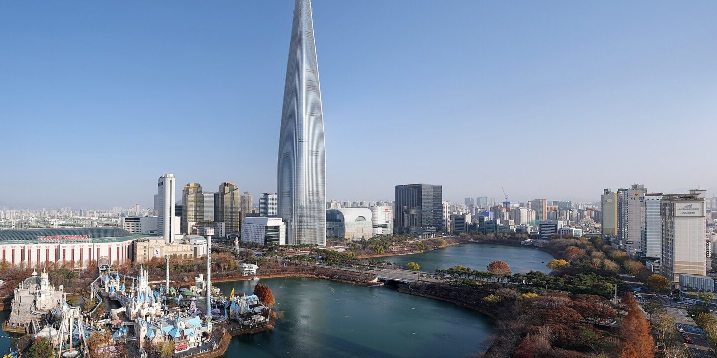Lotte World Tower rising above Seokchon Lake, with the white castle of Lotte World's Magic Island in the foreground under a clear blue sky