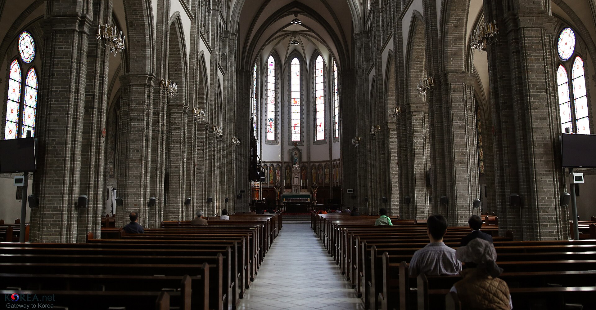 Nave of Myeongdong Cathedral with brick columns, stained-glass windows and wooden pews