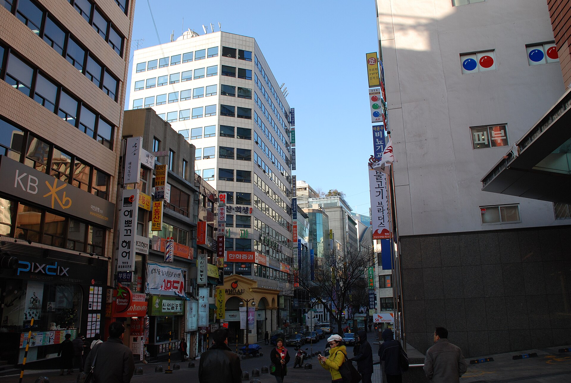 Narrow Myeongdong street lined with layered shop signs and mid-rise buildings under a clear sky