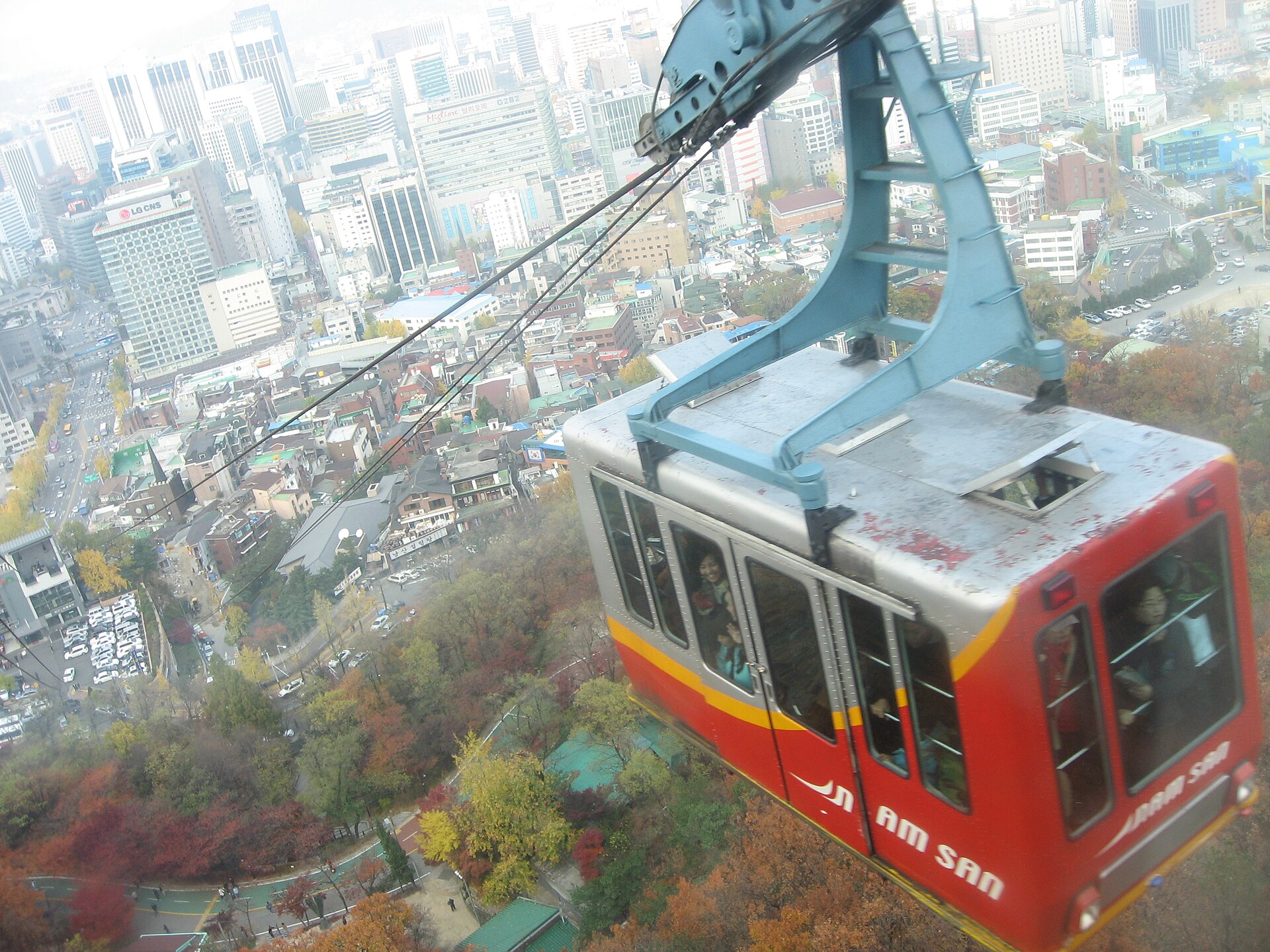 Red Namsan cable car cabin above autumn trees and central Seoul buildings