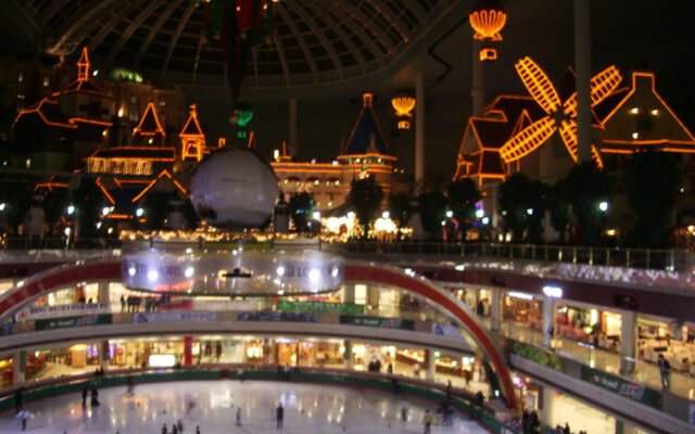 The glass-domed interior of Lotte World Adventure lit up at night, with an indoor ice rink and shopping galleries below