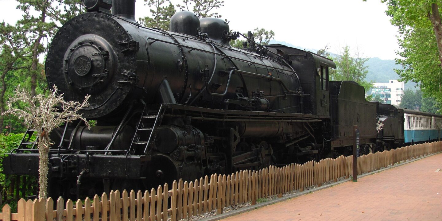 Old black steam locomotive on display beside a wide brick path in Seoul Children's Grand Park