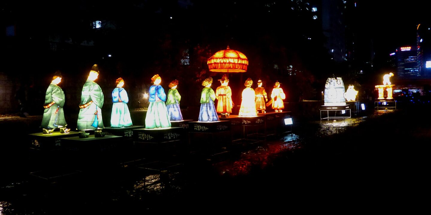 Illuminated lantern sculptures of figures in traditional Korean dress along Cheonggyecheon Stream at night