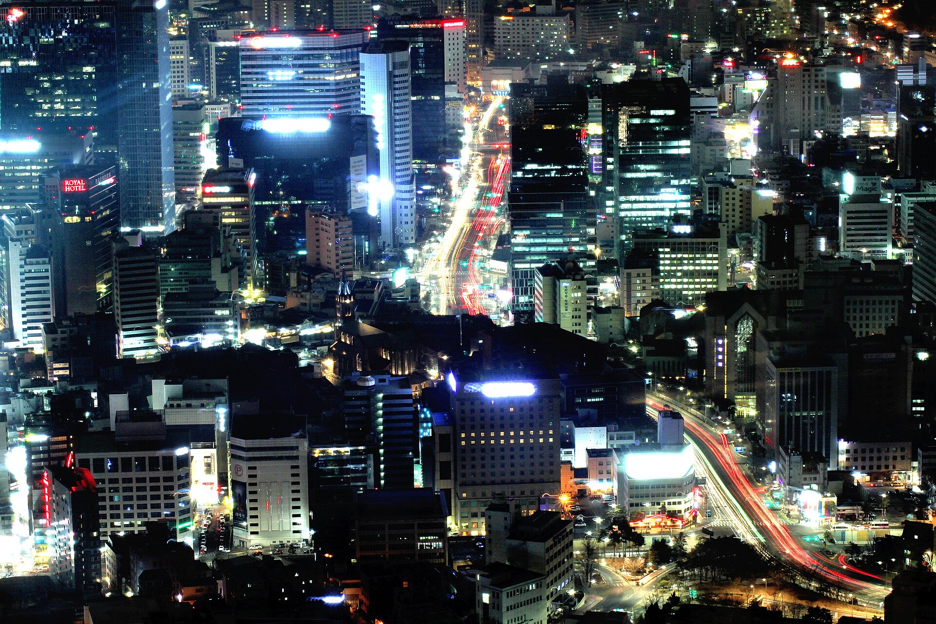 Central Seoul at night seen from high above, with lit office towers and streams of traffic along the main roads