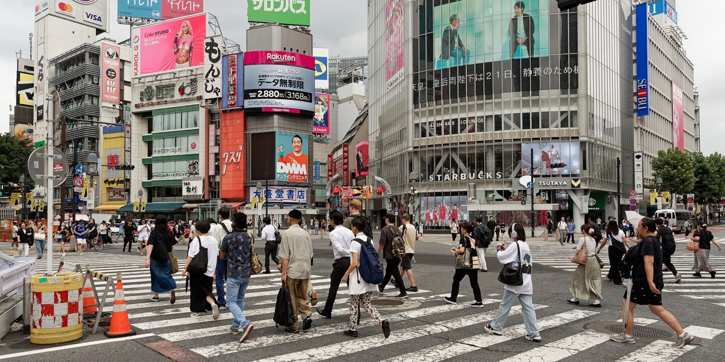 Pedestrians crossing the Shibuya scramble intersection in Tokyo beneath large advertising screens