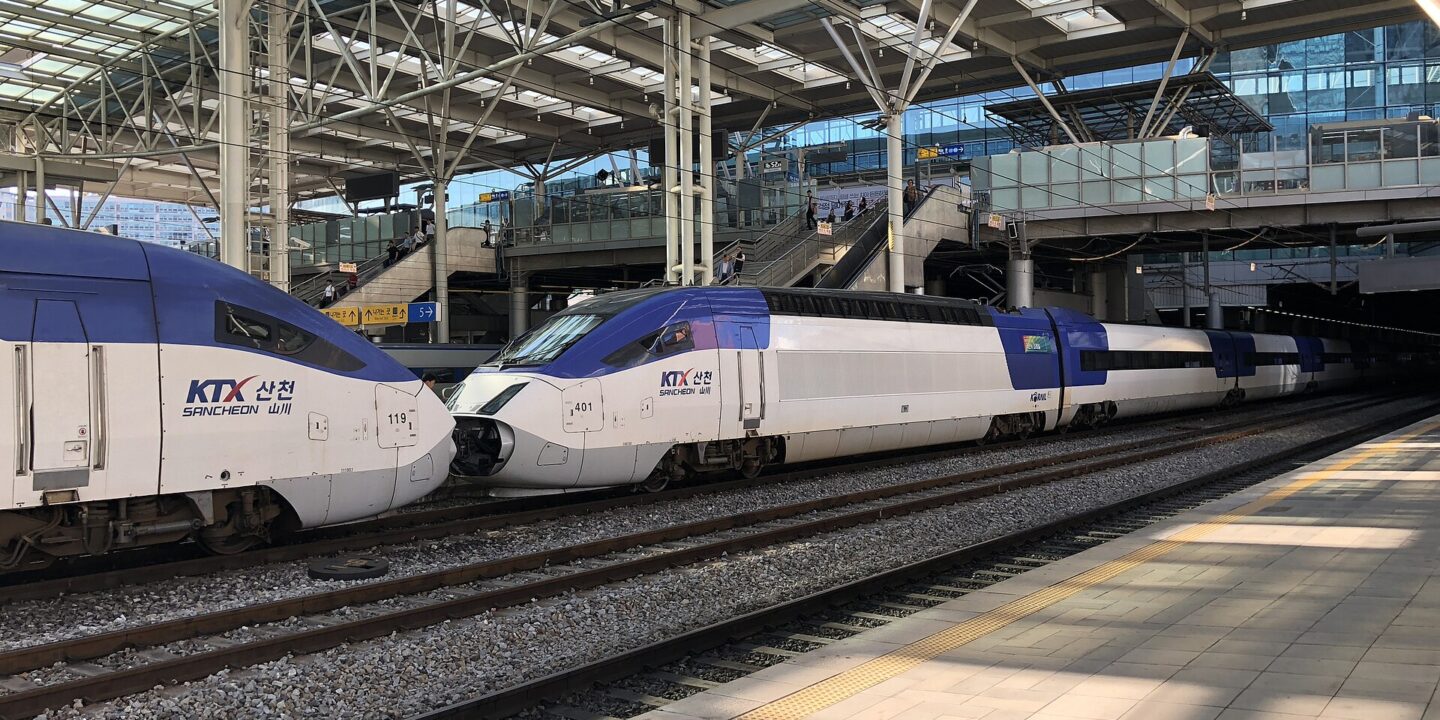 Two white high-speed trains with blue and grey noses side by side at a station platform under a steel roof