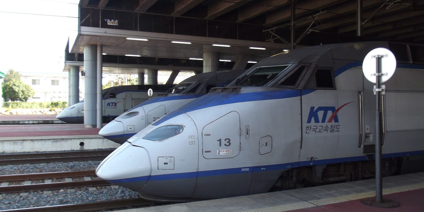 The noses of two white KTX high-speed trains with blue stripes side by side at a covered station platform