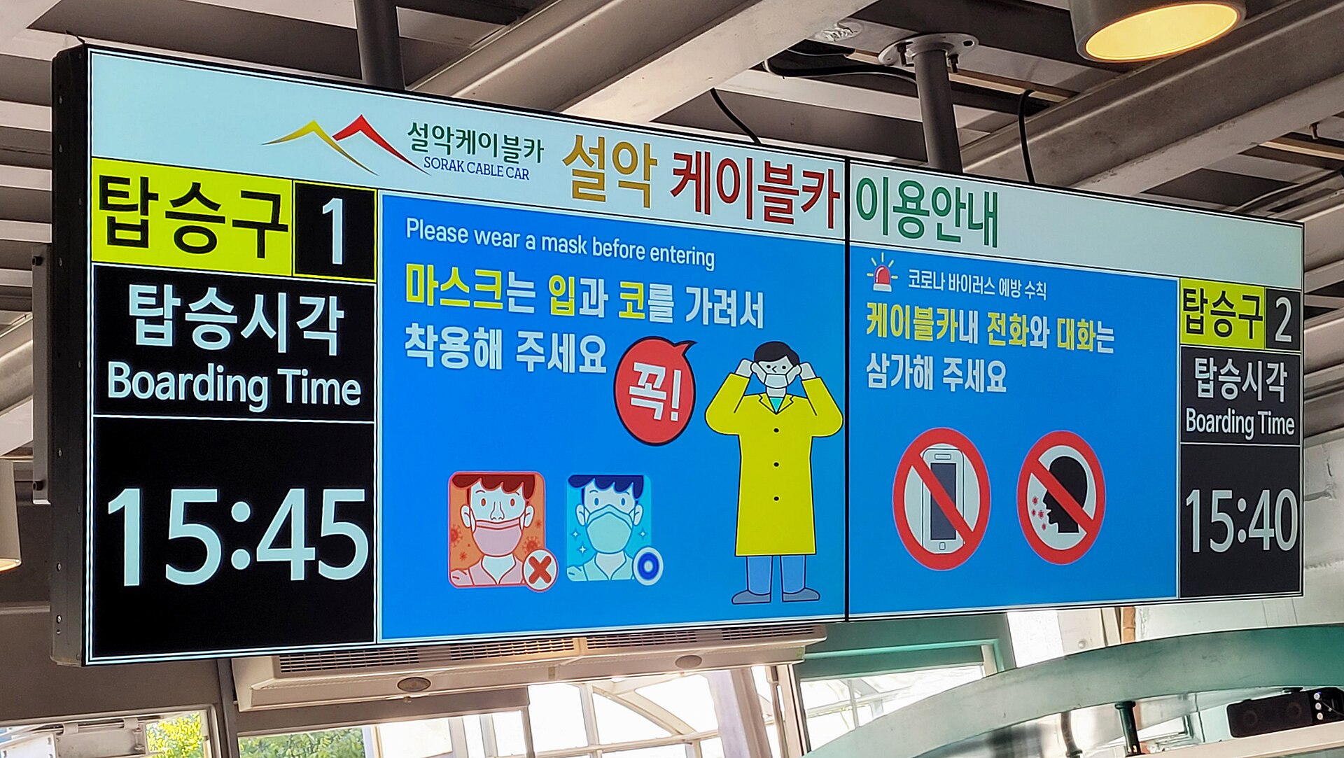 An overhead station display in Korean and English showing boarding times of 15:45 and 15:40 for two cable car boarding gates