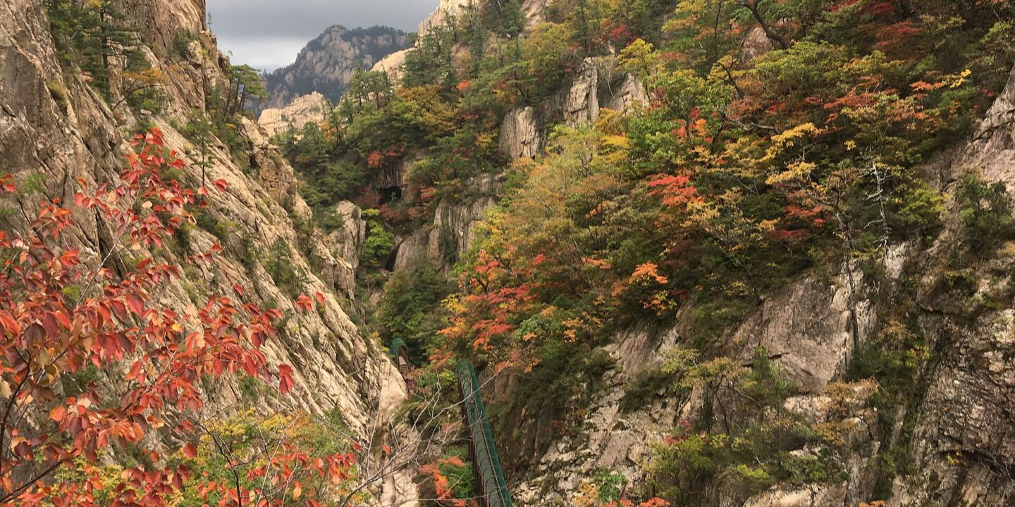 A narrow rocky gorge between steep granite walls covered in red, orange and yellow autumn trees, with a walkway along one side