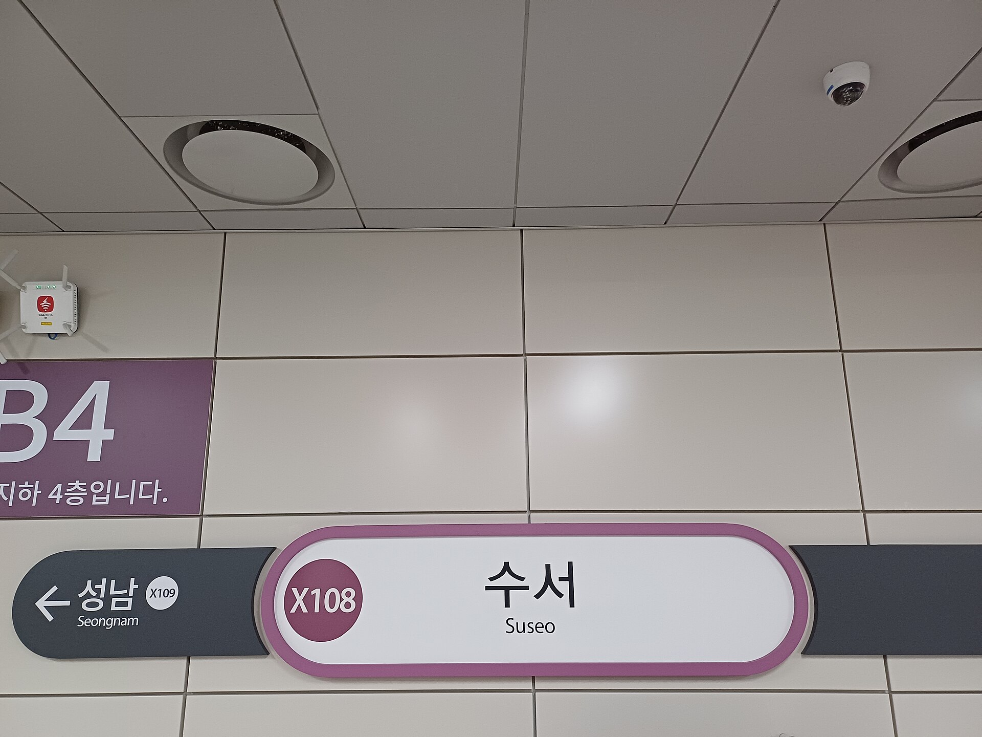 A white station nameboard reading Suseo in Korean and English with the code X108, next to a purple sign giving the floor as B4